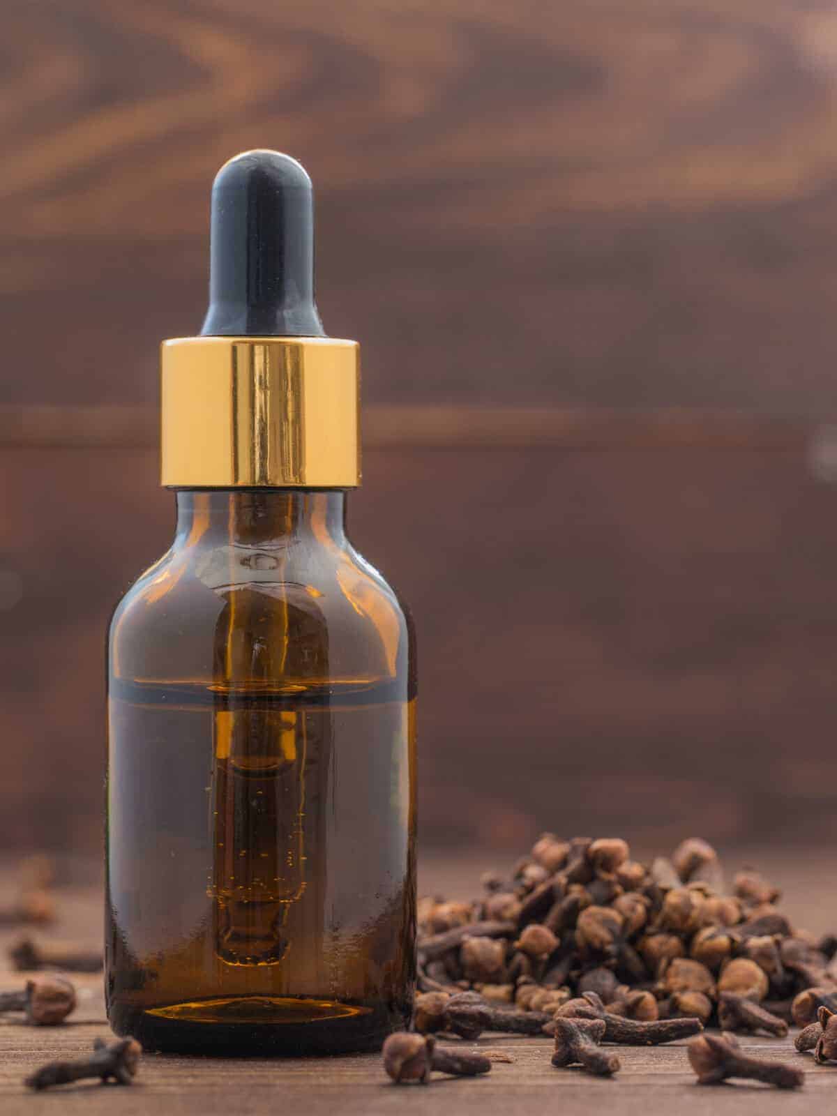 An amber bottle of clove essential oil surrounded by cloves.