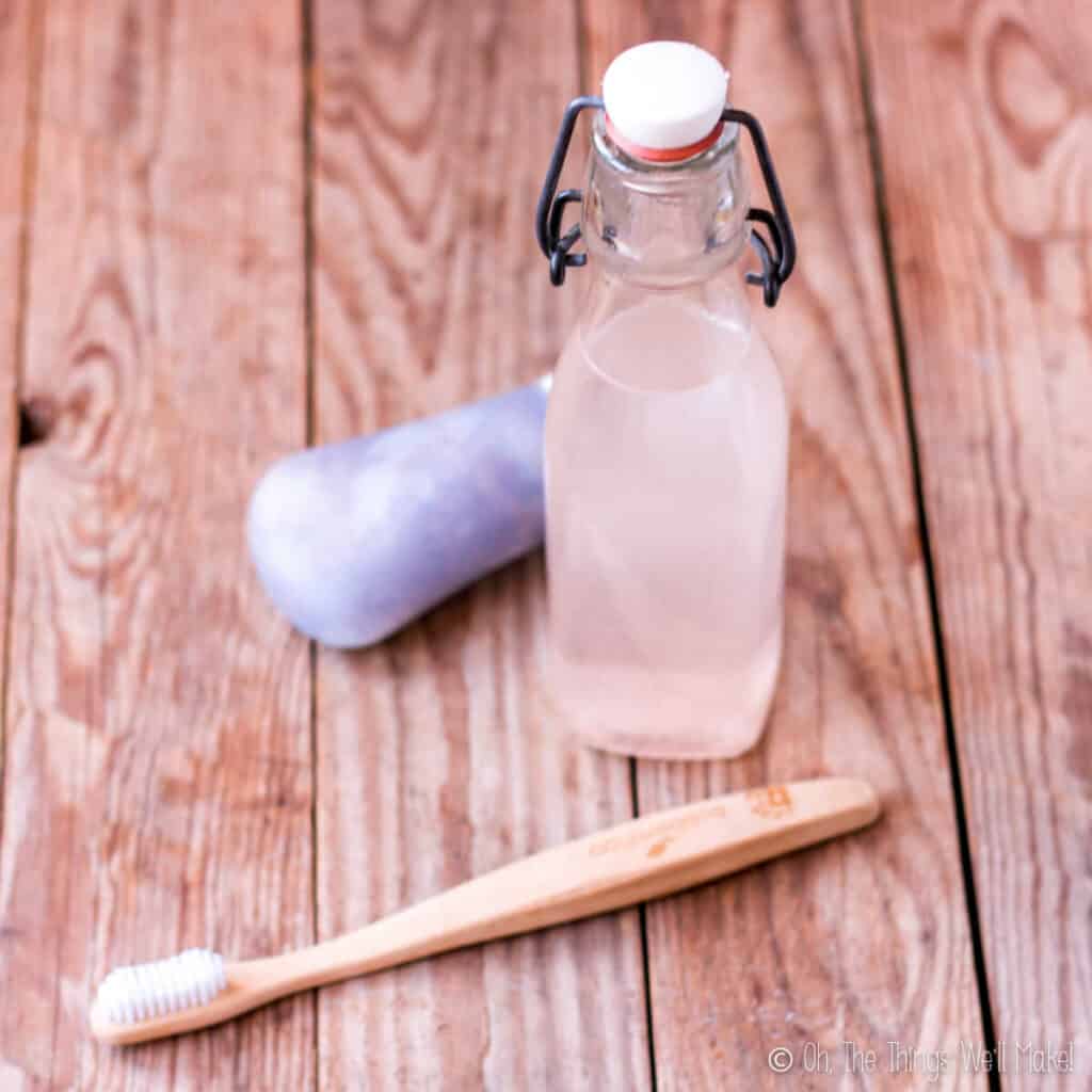 Bottle of homemade mouthwash with homemade toothpaste and a bamboo toothbrush