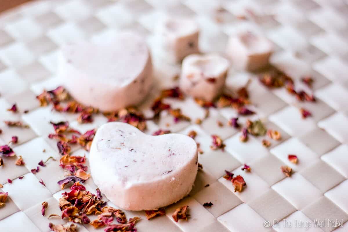 Several homemade rose petal bath bombs on a white woven placemat with some rose petals scattered on it too.