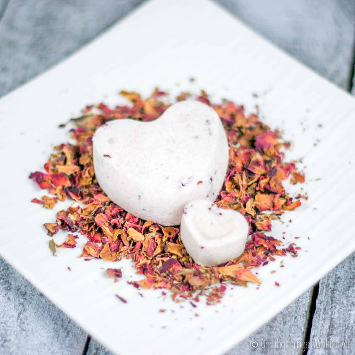 Close up of two heart shaped bath bombs. A large one and a small one placed on a plate full of rose petals.