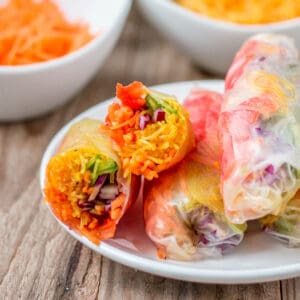 Closeup of a spring roll that has beeb cut in half on a plate showing the colorful rainbow of vegetables inside.