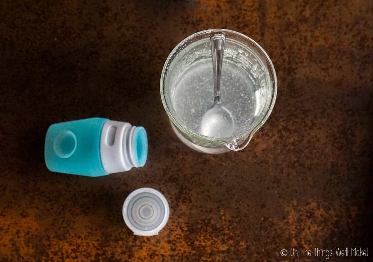 overhead view of a homemade sanitizer gel in a beaker, ready to pour into a silicone travel tube next to it. 