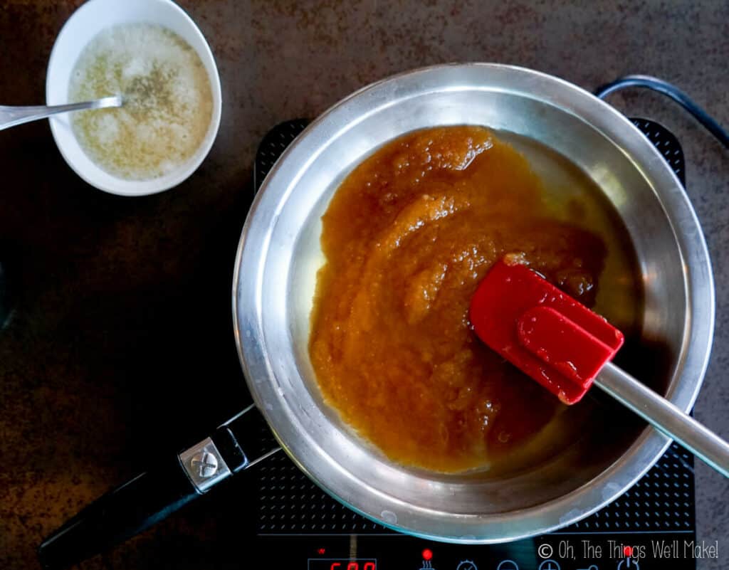 Overhead view of a honey and water mixture in a pan with a bowl of gelatin and water above it. 
