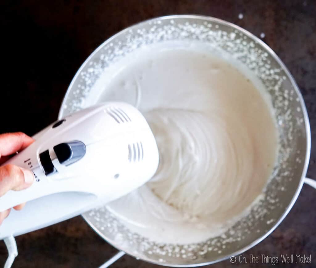 Overhead view of an electric beater whipping the honey gelatin mixture more fully. It has increased in volume and It's almost white in color.