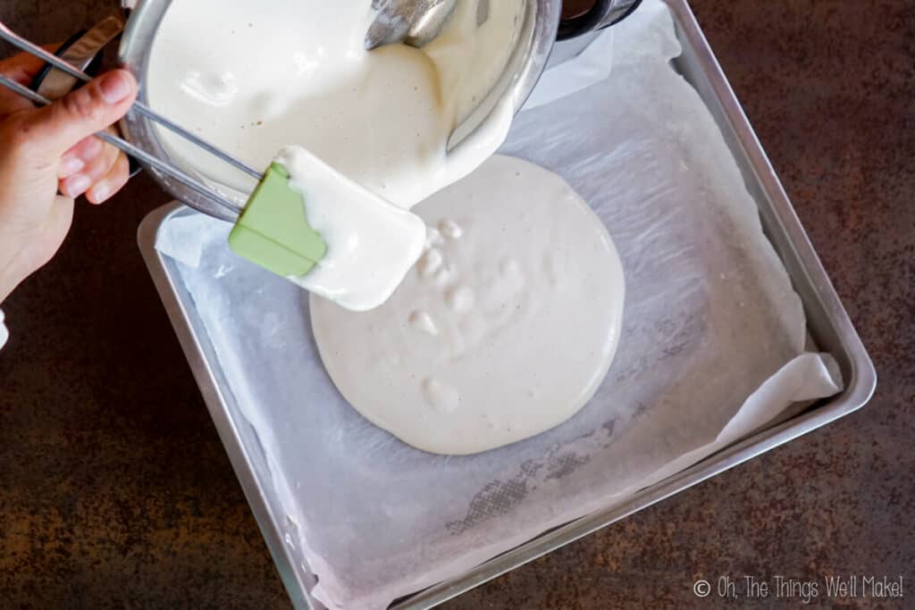 Pouring a marshmallow mixture into a pan lined with baking paper.