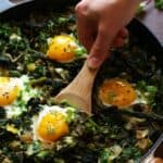 scooping up the egg and greens of shakshuka with a wooden spoon