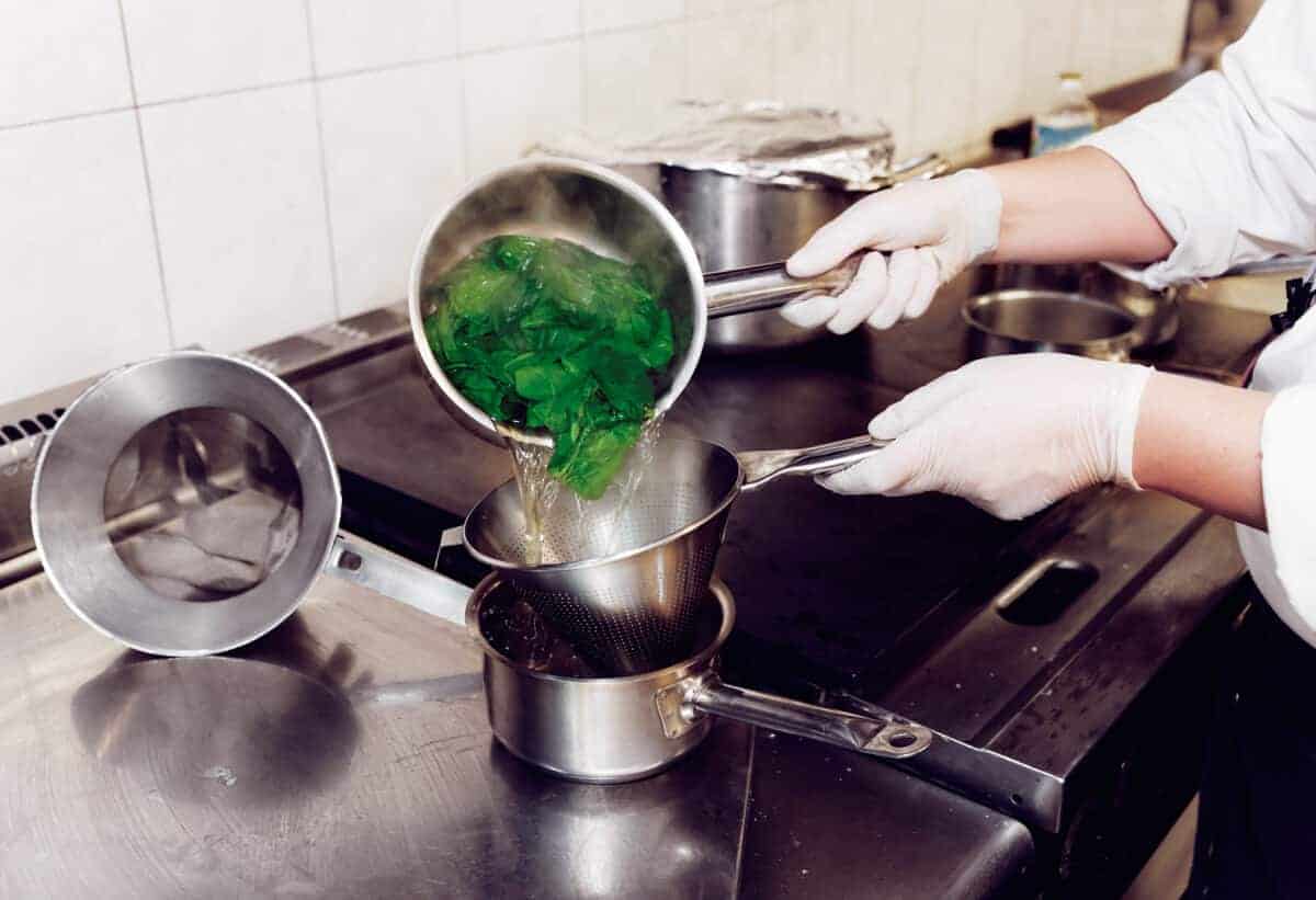 pouring boiled spinach through a strainer
