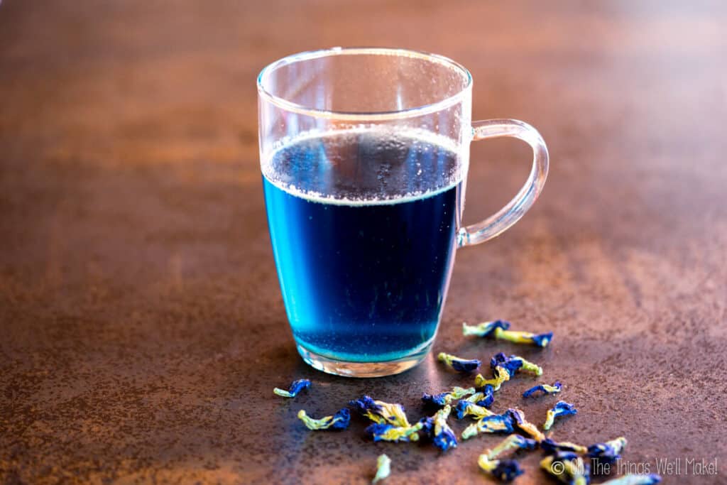 a cup of blue tea with butterfly pea flowers around it.