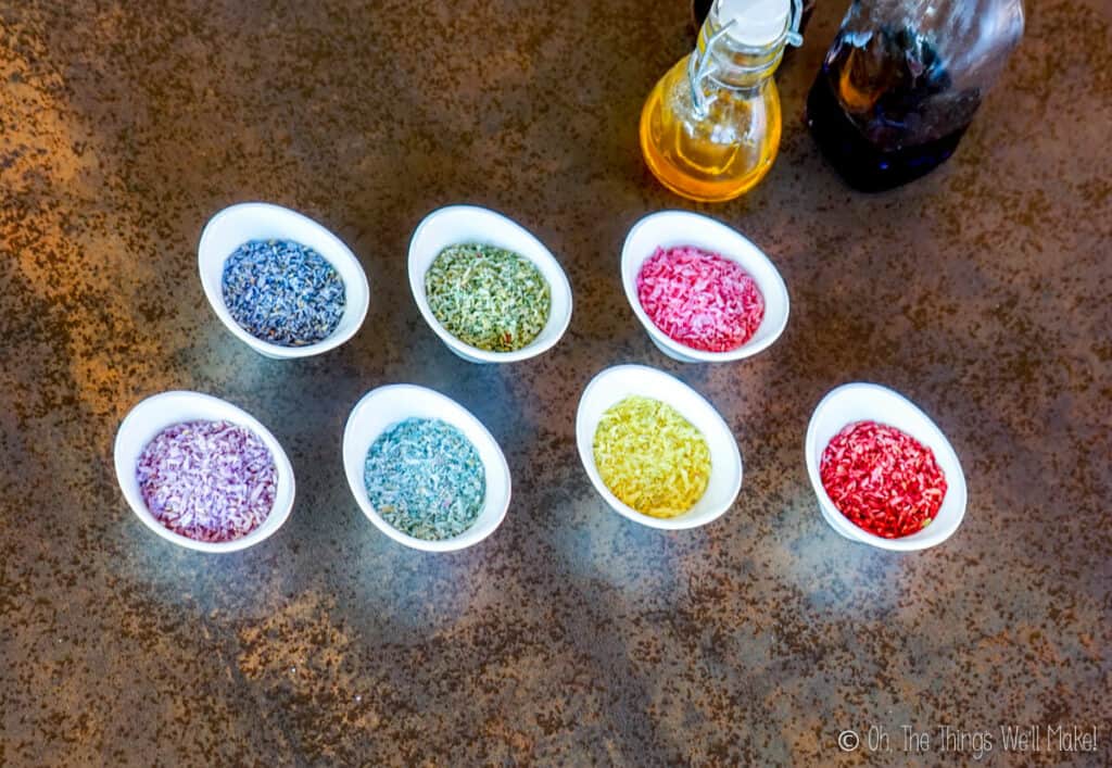 Overhead view of 7 small bowls filled with coconut sprinkles in a rainbow of colors. 