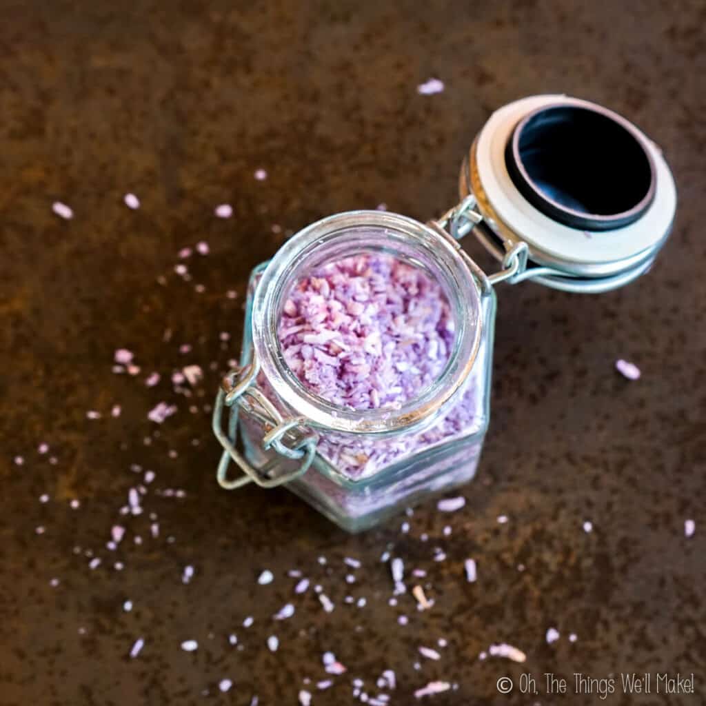Overhead view of purple coconut sprinkles in an open jar, with more sprinkles over the surface below it.