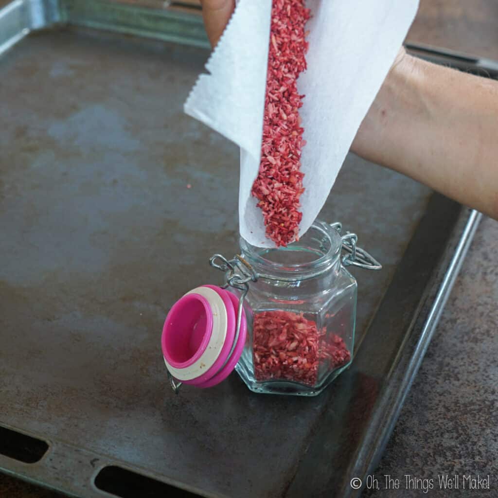 Pouring pink sprinkles from a rolled up paper into a glass jar