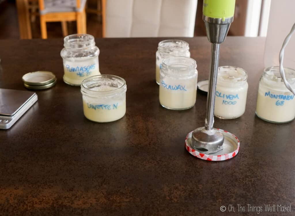 Several jars filled with homemade lotions next to an immersion blender