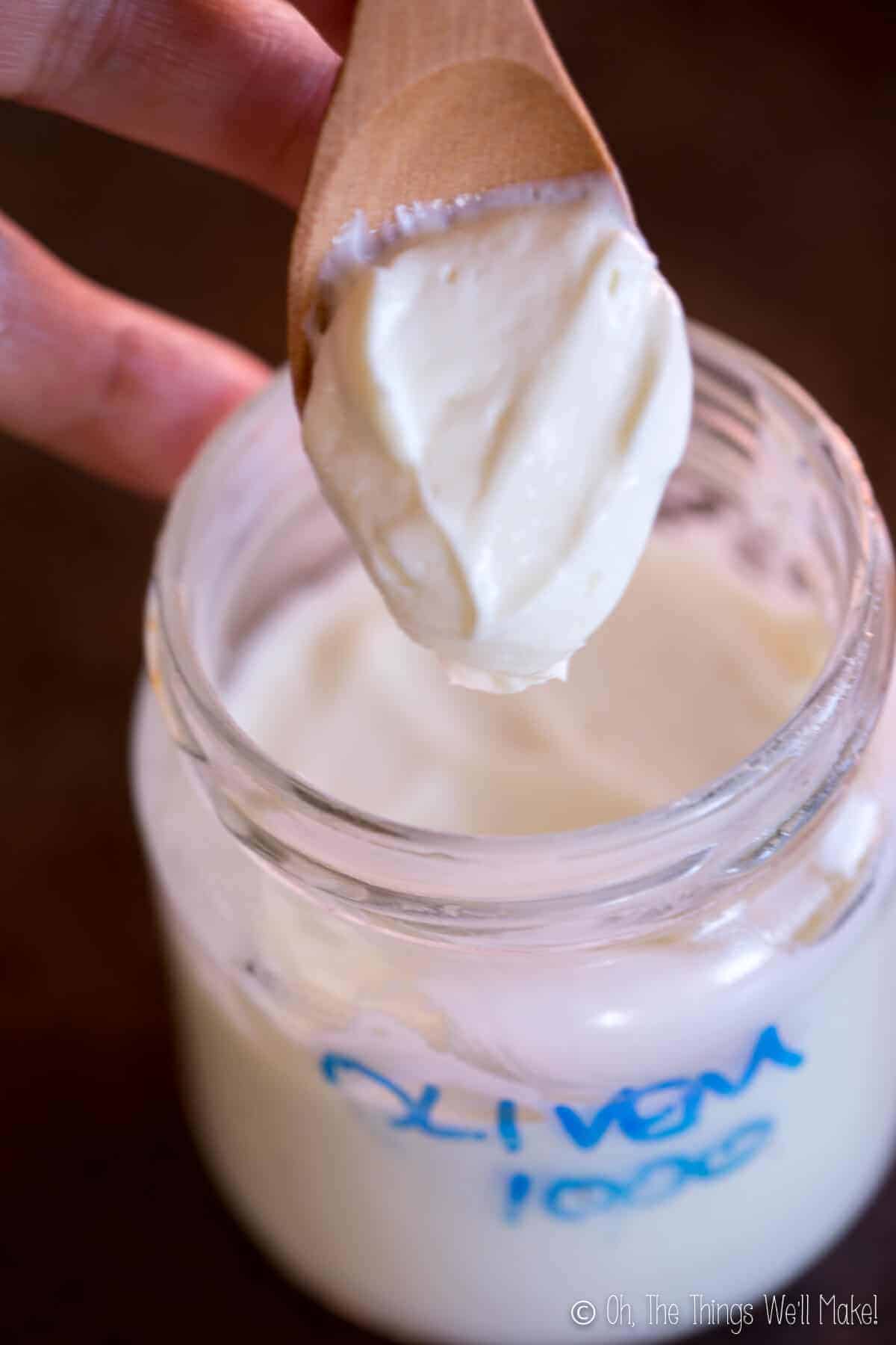 A wooden spoon in a jar of lotion made with Olivem 1000, showing the texture.