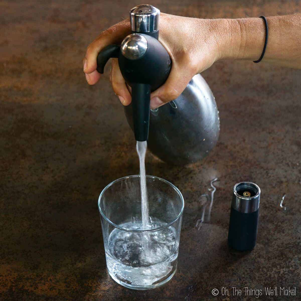 filling a glass with sparkling water by pressing on the lever of a soda siphon.