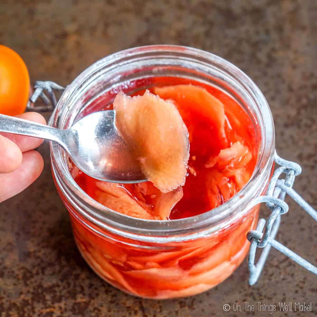 Removing a slice of pickled ginger from a jar of it with a spoon