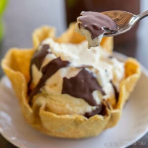 Spooning up some ice cream with.a hard chocolate topping on it from a waffle bowl of ice cream with shell topping.