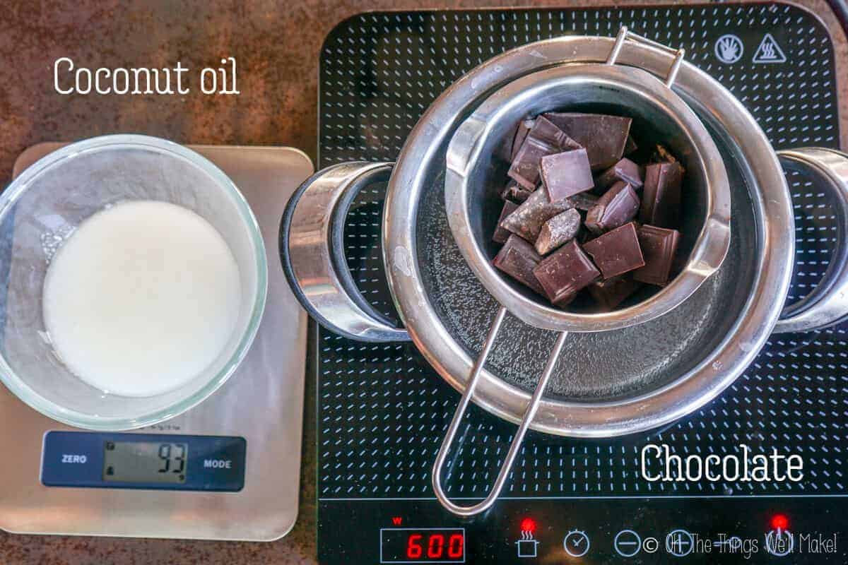 Top view of chopped chocolate inside a double broiler and a container of coconut oil on a measuring scale the left side.