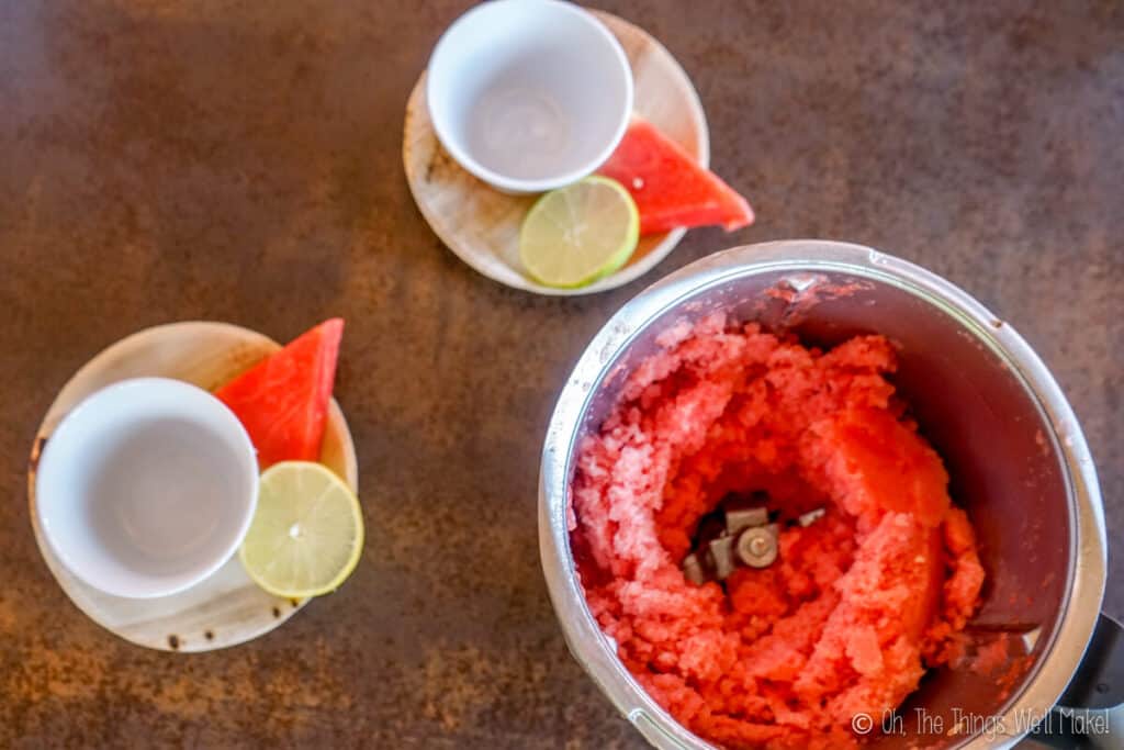 2 empty bowls next to a food processor filled with watermelon sorbet.