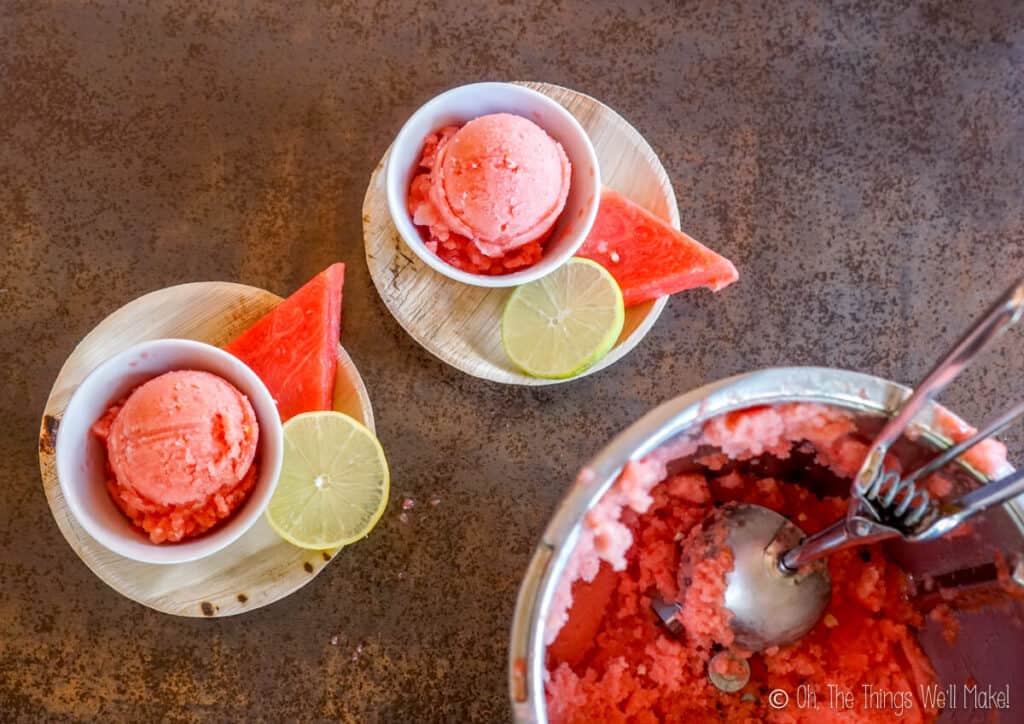 Overhead view of watermelon sorbet in bowls next to a food processor container filled with more sorbet and an ice cream scoop.