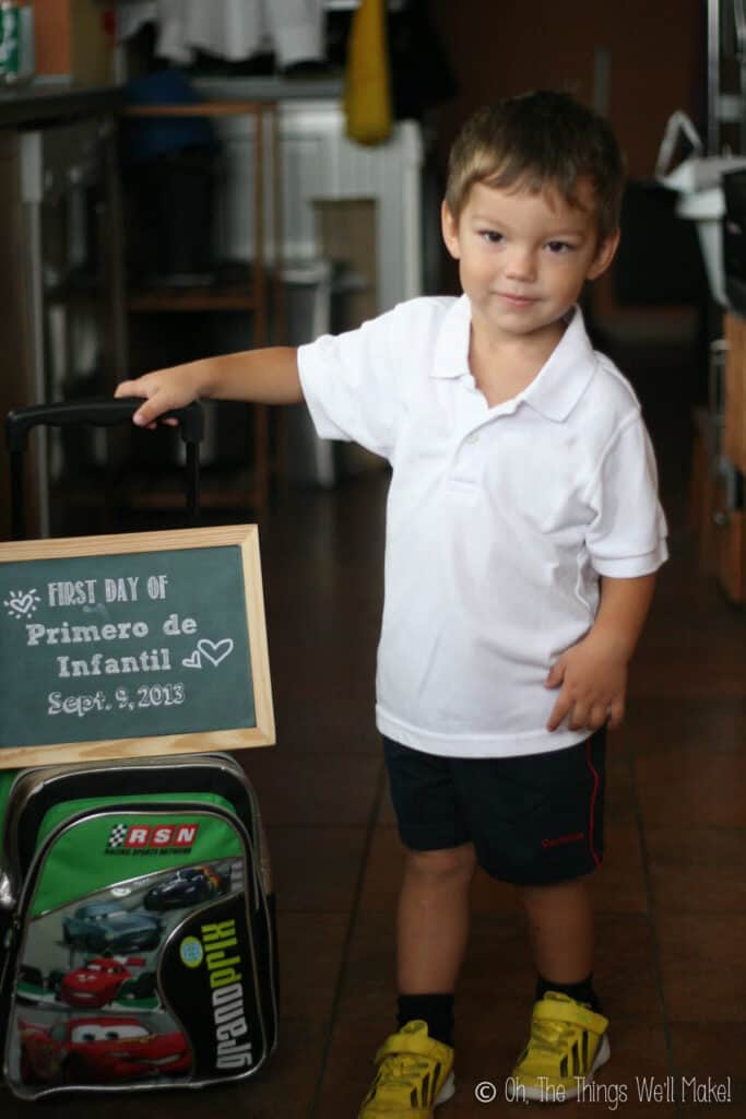 2 year old boy holding up a chalkboard sign on his first day of school.