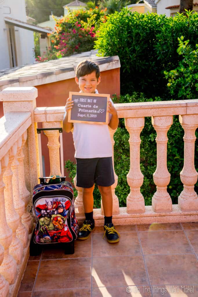 8 year old boy holding up a chalkboard sign on his first day of school.