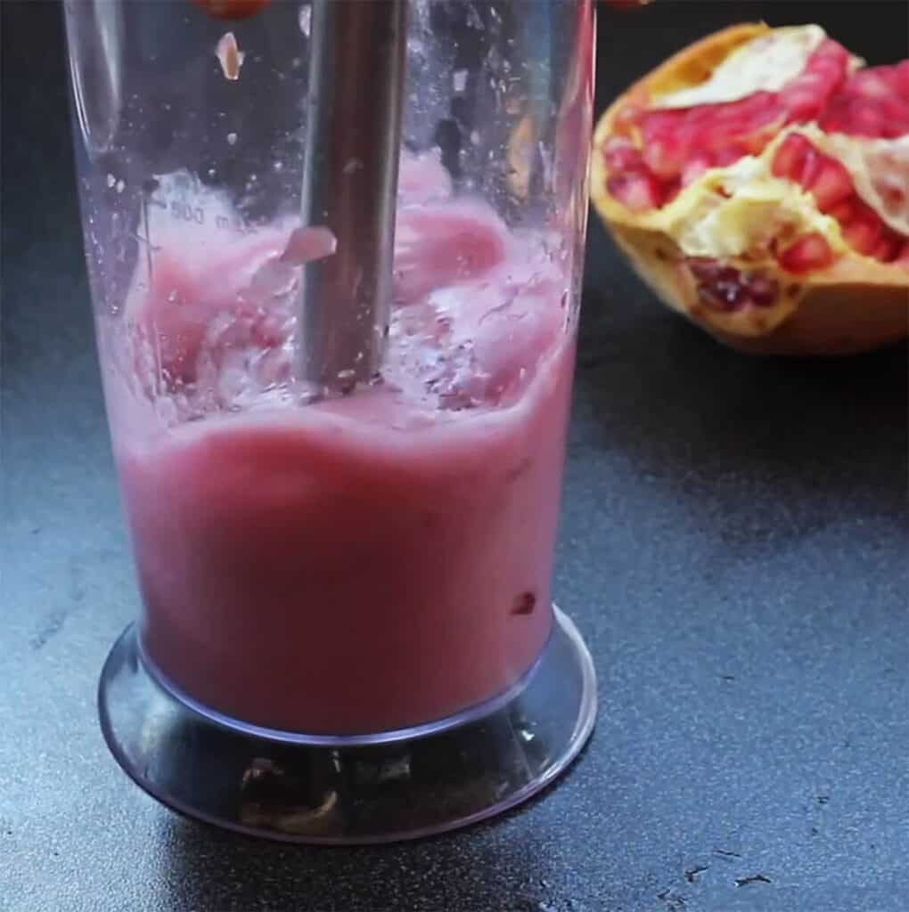 A handheld blender blending pomegranate seeds to release their juice.