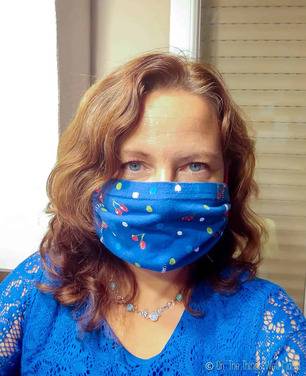 A woman wearing a blue jersey face mask which has been painted with cherries and polka dots