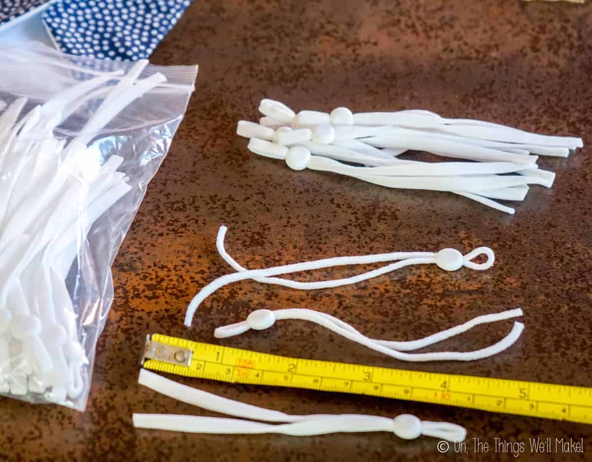 Overhead view of several pieces of white elastic cording with cord locks on them, near an extended measuring tape