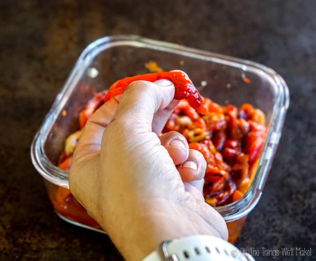 Holding a piece of red pepper and pressing a thumb into the center of the piece.