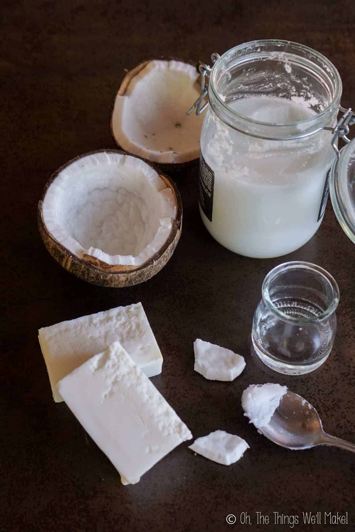 An open coconut next to a jar of solid coconut oil and a smaller jar of liquid coconut oil. All are next to 2 bars of coconut oil soap.