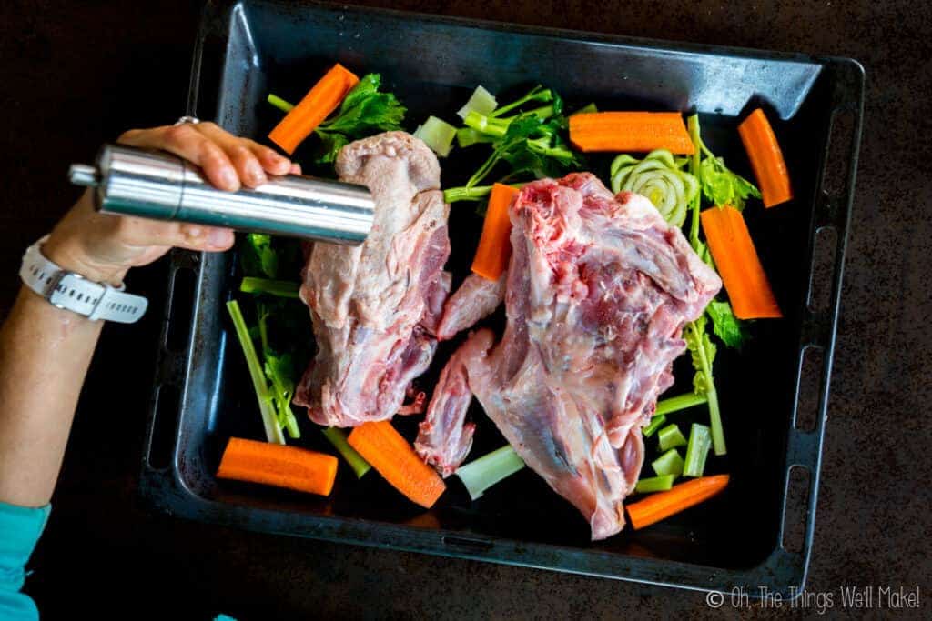 Adding pepper to a turkey carcass on a tray with veggies