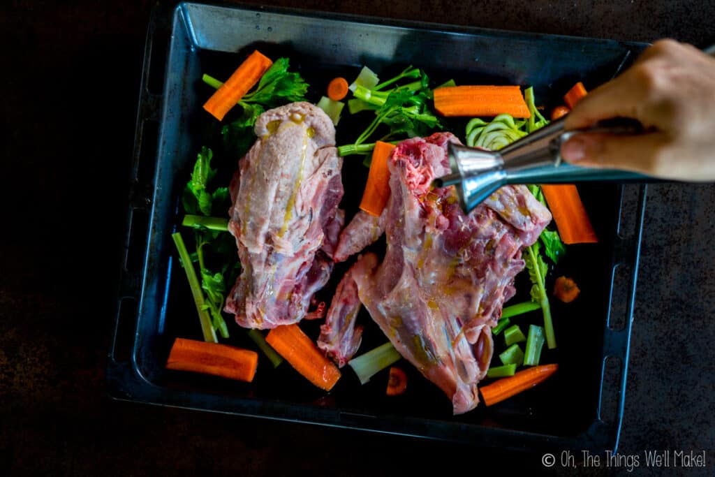 Pouring oil over a turkey carcass on a tray with veggies