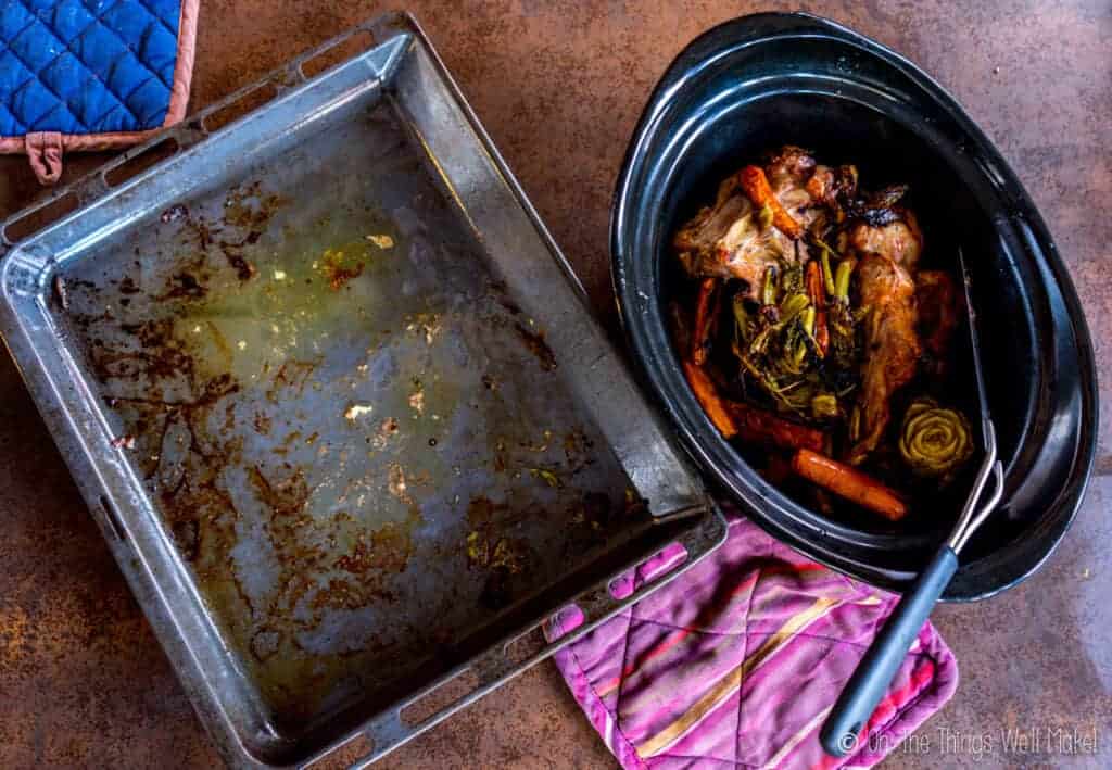 A roasted turkey carcass in a slow cooker next to an empty baking tray.
