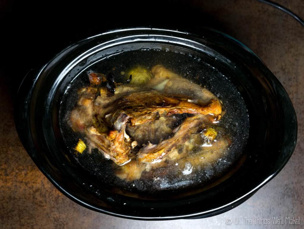 Overhead view of a slow cooker with turkey bones and stock.