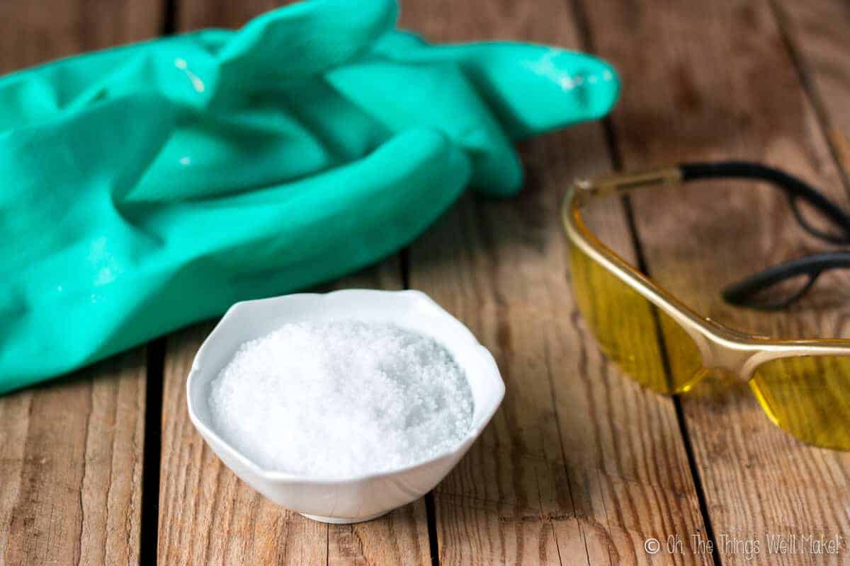 A bowl of lye in front of safety glasses and gloves