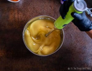An immersion blender blending a yellow liquid in a bowl.