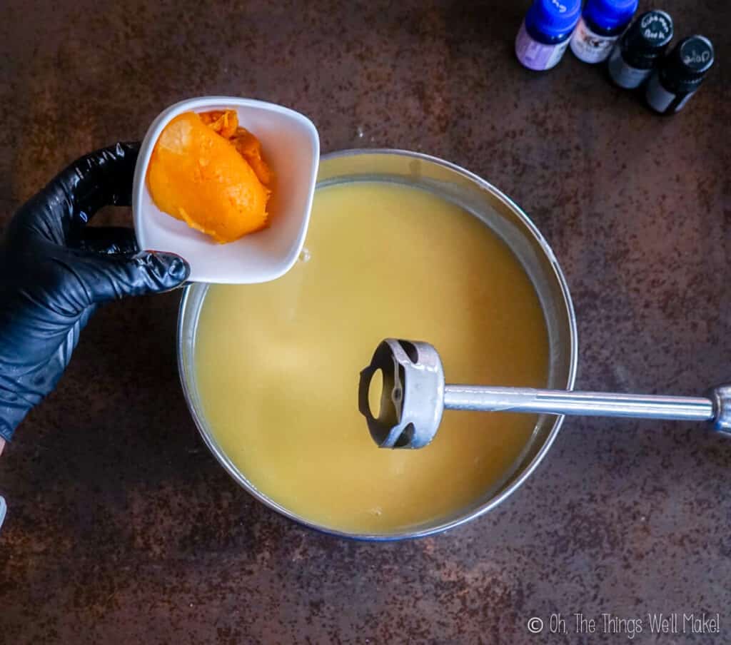 A small bowl with pumpkin puree being poured into a bowl with a soap mixture