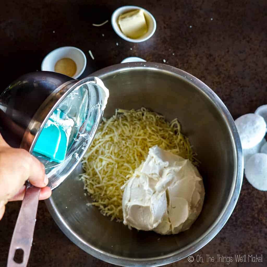 Adding cream cheese to a bowl with shredded cheeses