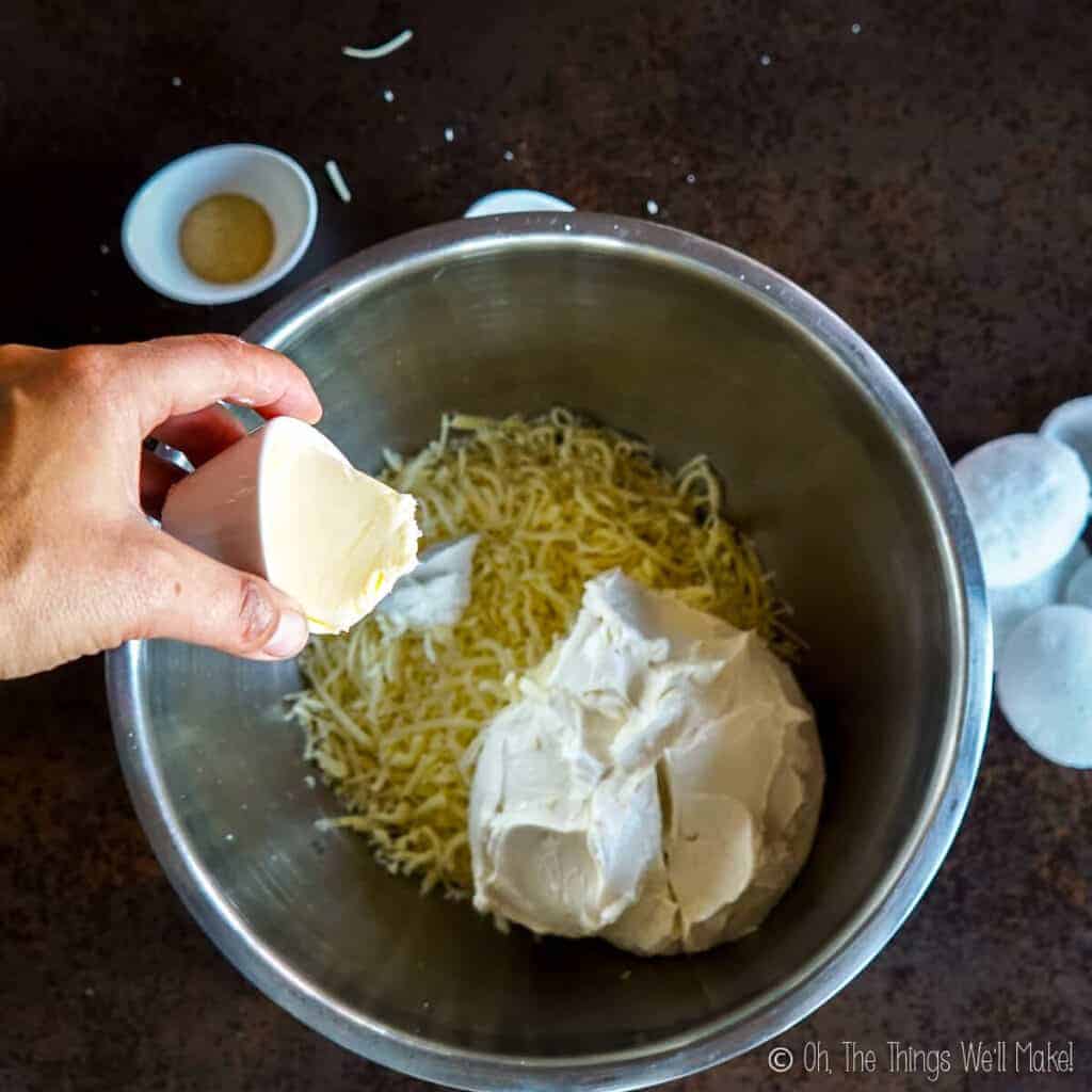 Adding butter to the bowl with the cheeses