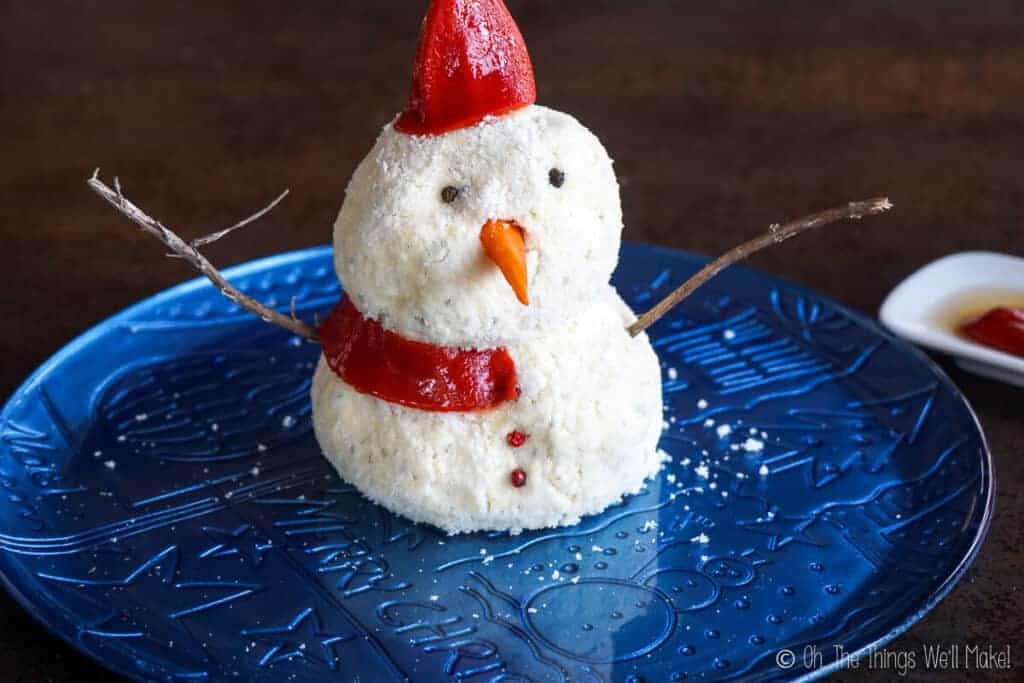 Snowman cheese ball with a roasted red pepper hat and a strip of roasted red pepper forming half of a scarf.