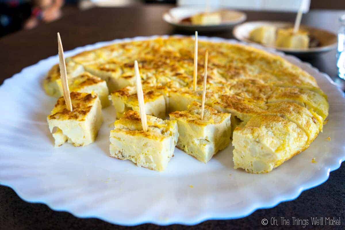 A Spanish tortilla on a plate cut into cubes with toothpicks in several of the pieces.
