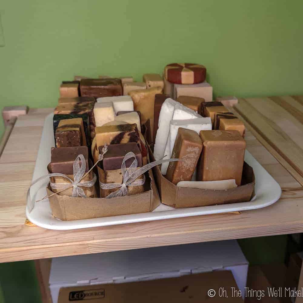 Overhead view of many groups of soaps curing on a tray that is sitting on the top shelf of a bookcase.