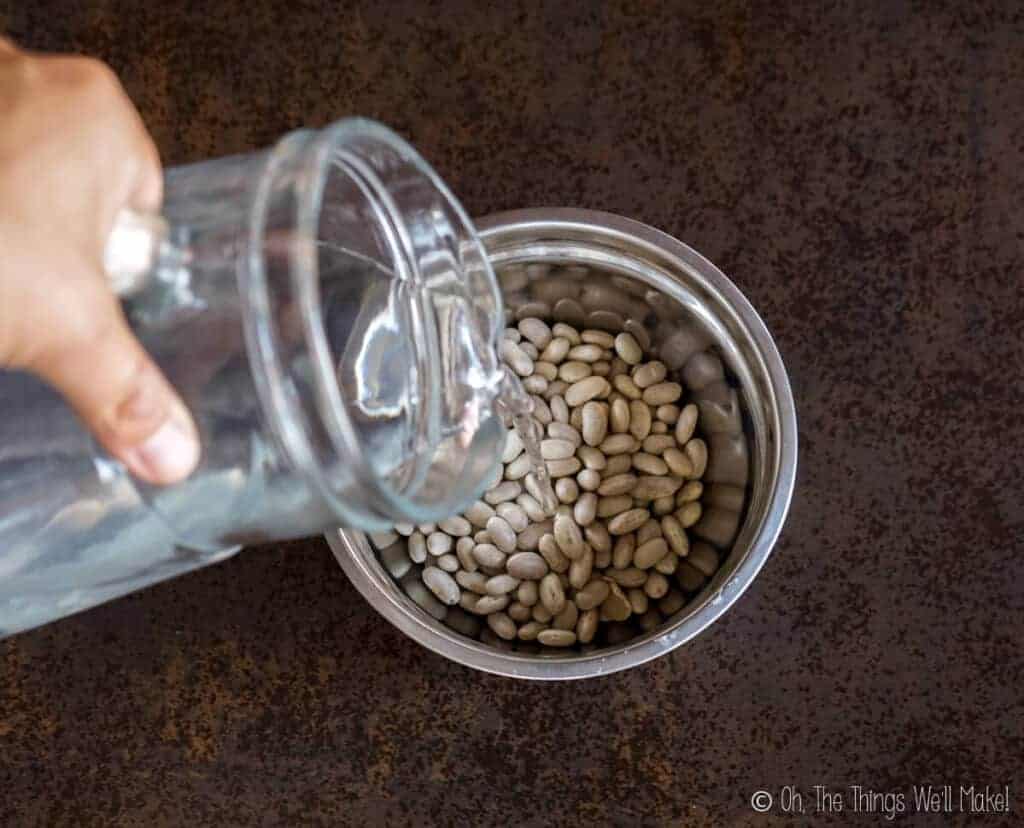 Pouring water into a bowl with white beans