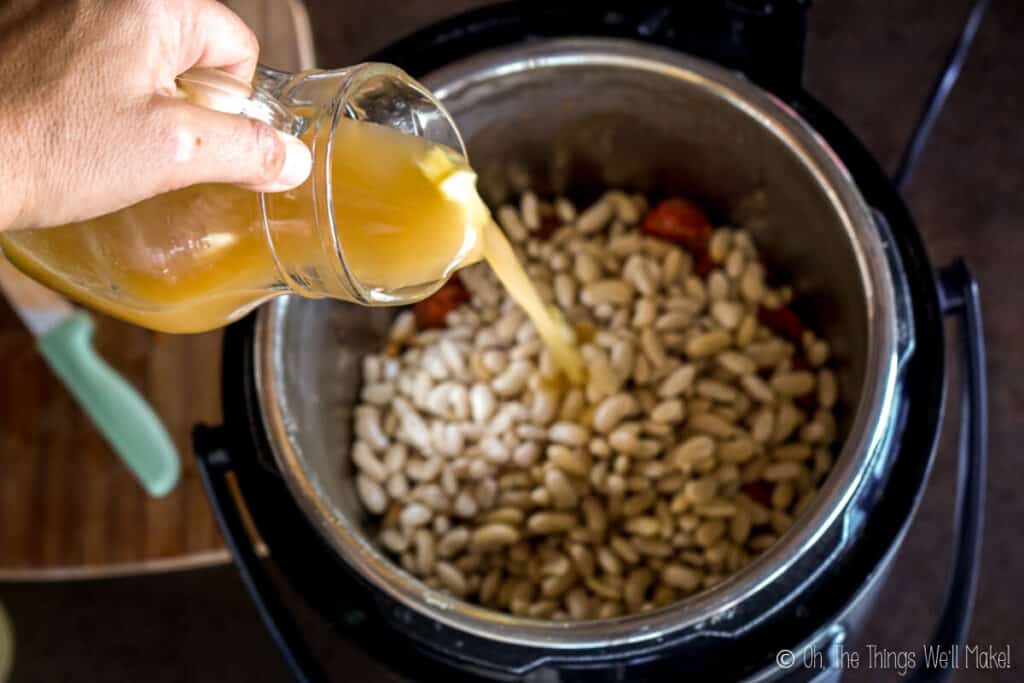 Pouring broth into the pressure cooker with the beans