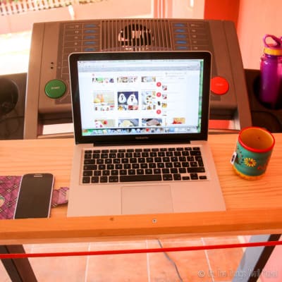 A computer, a phone, and a mug on a removable desk on a treadmill.