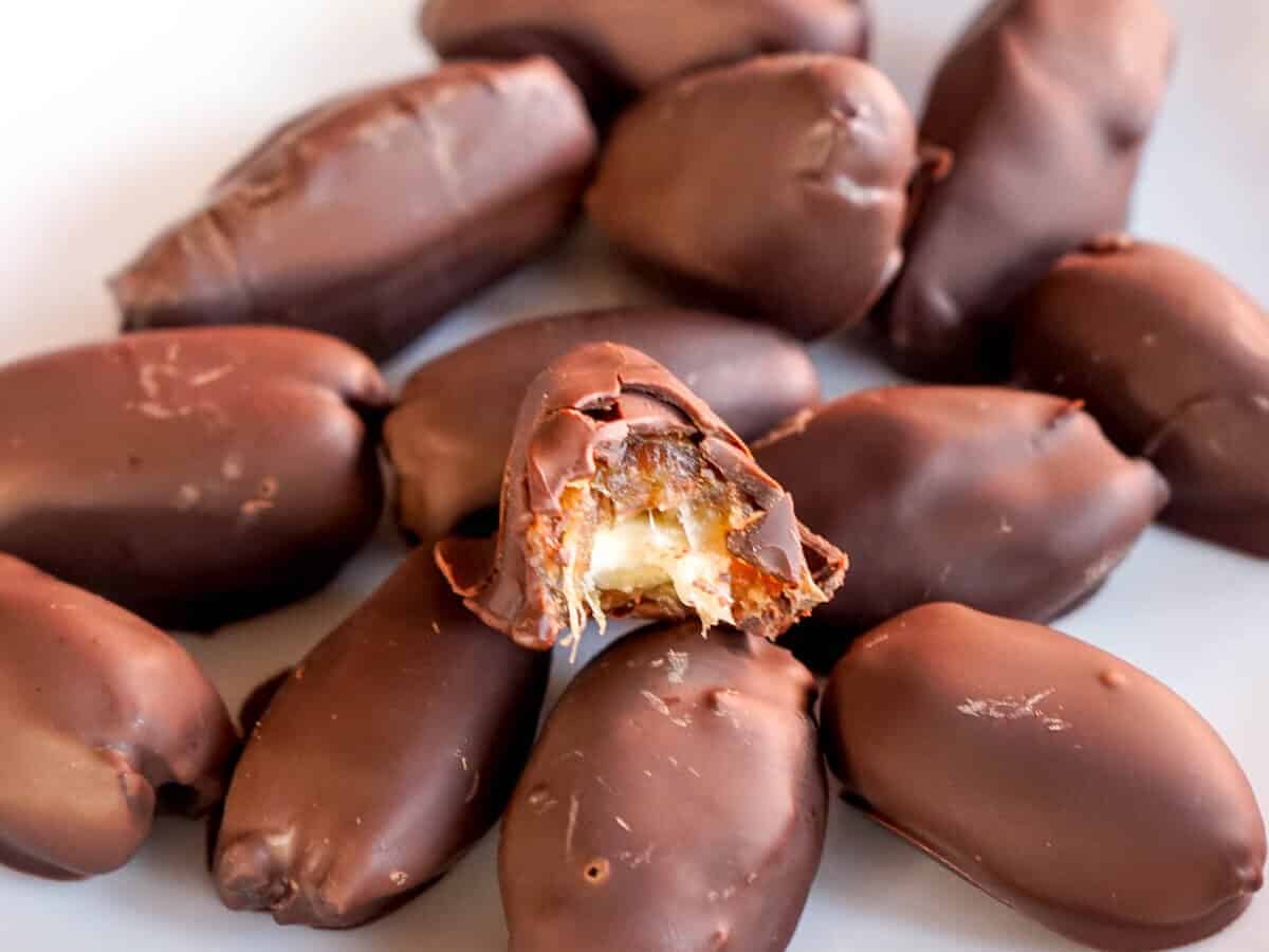 Closeup of a pile of chocolate dates with almonds, focusing on one that is bit open