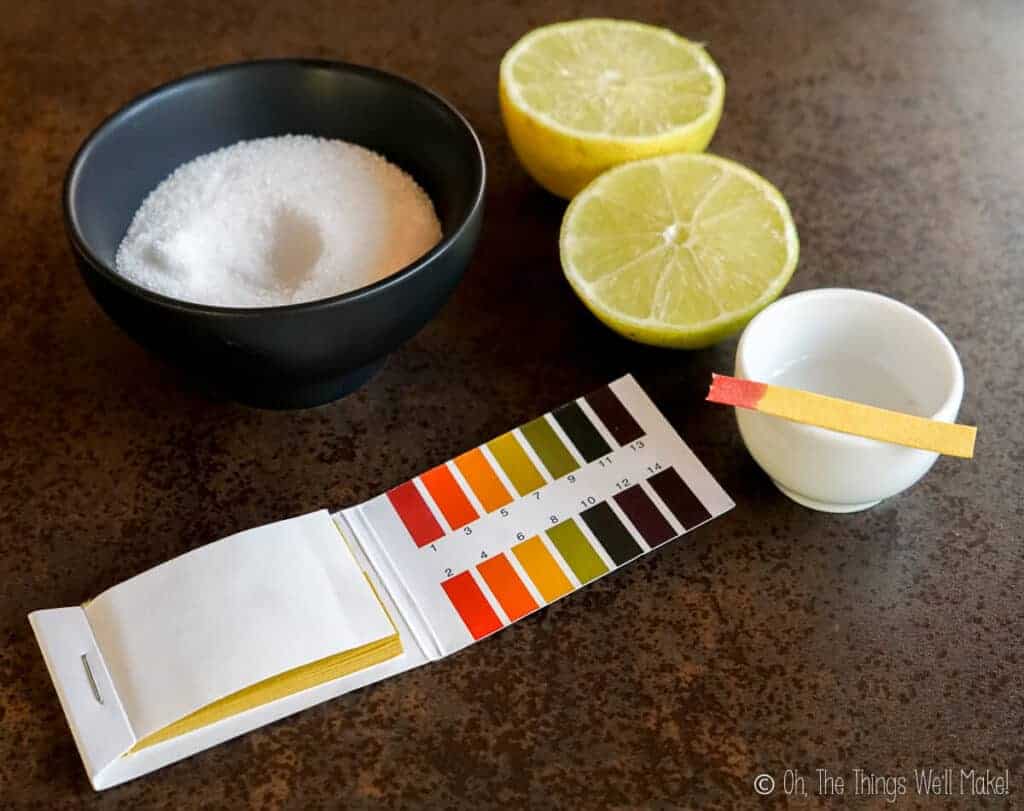 citric acid in a bowl next to a cut lemon and pH test strips