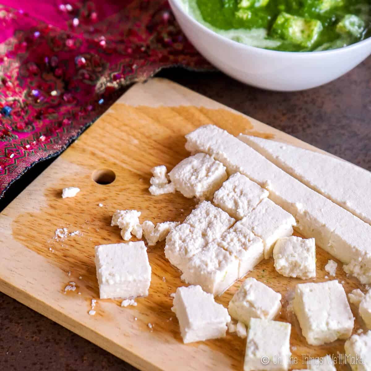 Overhead view of cut cubes of homemade paneer on a bamboo cutting board