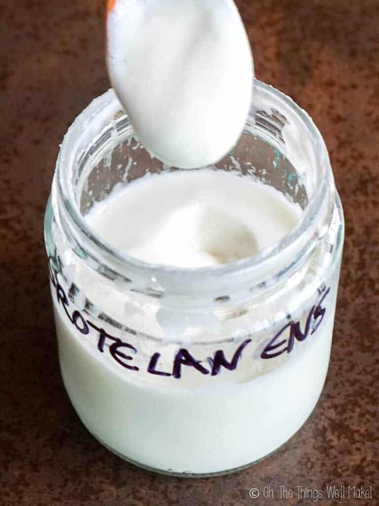 A jar of a lotion made with Protelan ENS emulsifier. This lotion is thicker and some of the lotion is shown on a spoon over the jar.