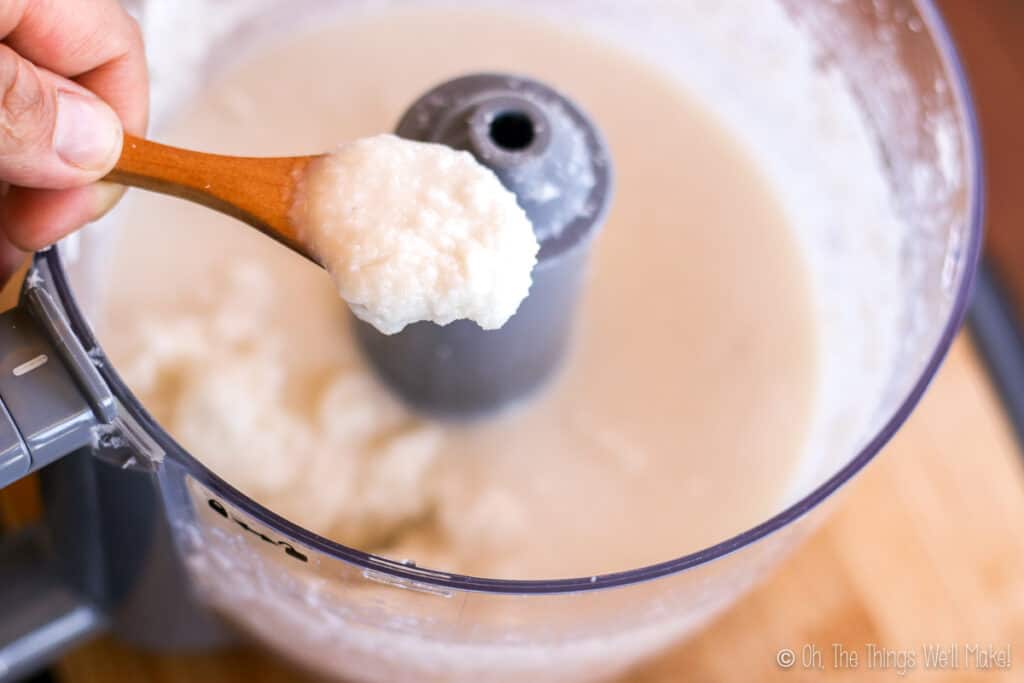 A spoonful of coconut butter held over a food processor with coconut butter